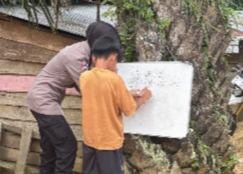 Bripda Nia Kurnia membimbing seorang anak SAD belajar menulis di papan tulis portabel yang dipasang di batang pohon, Desa Bungku, Kecamatan Bajubang, Batanghari, Jambi. Dok. Humas Polsek Bajubang)