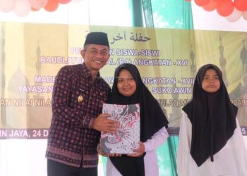 Wakil Bupati Muaro Jambi Junaidi H. Mahir menyerahkan penghargaan kepada siswa Madrasah Darul Amal dalam acara pelepasan siswa di Desa Suko Awin Jaya, Sabtu (21/6/2025). (Dok. Kominfo)