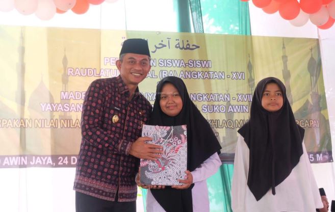 Wakil Bupati Muaro Jambi Junaidi H. Mahir menyerahkan penghargaan kepada siswa Madrasah Darul Amal dalam acara pelepasan siswa di Desa Suko Awin Jaya, Sabtu (21/6/2025). (Dok. Kominfo)
