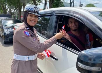 Personel Satlantas Polresta Jambi membagikan bendera Merah Putih kepada pengendara mobil saat kegiatan simpatik menyambut HUT ke-80 RI di Simpang Empat Museum, Kota Jambi, Selasa (12/8/2025). (Dok. Nahar)