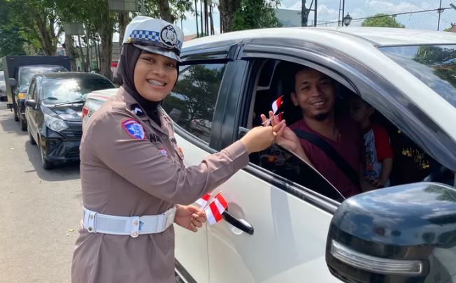 Personel Satlantas Polresta Jambi membagikan bendera Merah Putih kepada pengendara mobil saat kegiatan simpatik menyambut HUT ke-80 RI di Simpang Empat Museum, Kota Jambi, Selasa (12/8/2025). (Dok. Nahar)