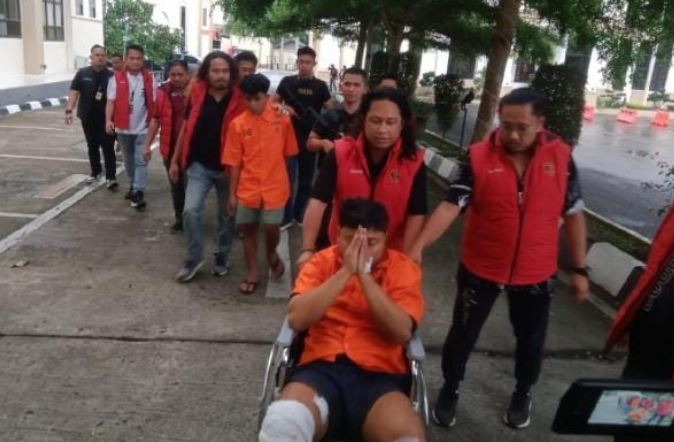 Petugas kepolisian menggiring dua tersangka kasus pembunuhan sopir taksi online Maxim di Jambi. Salah satu tersangka, Hafif (22), menggunakan kursi roda akibat amputasi kaki dan masih menjalani perawatan di RS Bhayangkara Jambi, Selasa (12/8/2025). (Dok. Nahar)