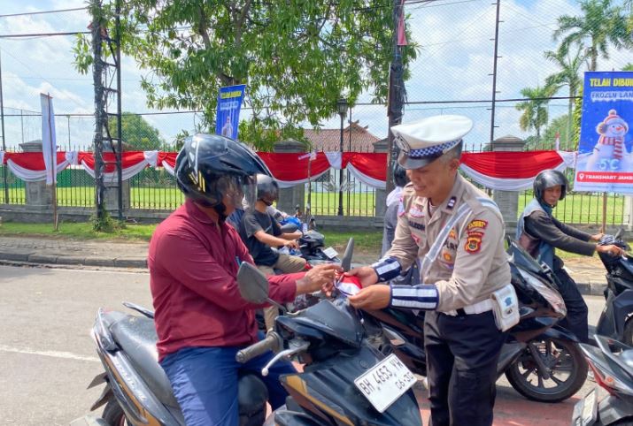 Personel Satlantas Polresta Jambi membagikan bendera Merah Putih kepada pengendara sepeda motor di kawasan simpang empat Museum, Jalan Slamet Riyadi, Kota Jambi, Kamis (14/8/2025) (Dok. Daus)