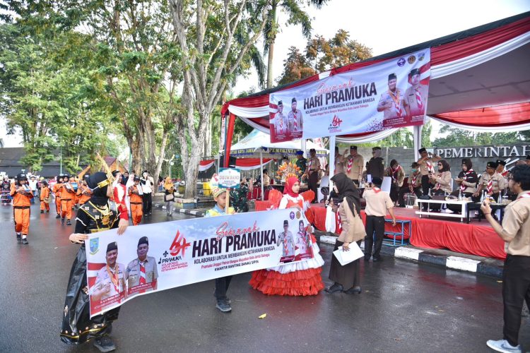 Peserta dari Kwartir Ranting Danau Sipin membawa spanduk bertema Semarak Hari Pramuka ke-64 saat melintas di depan panggung kehormatan di kawasan Tugu Keris Siginjai, Kota Jambi, Sabtu (9/8/2025). (Dok.Stepanus)