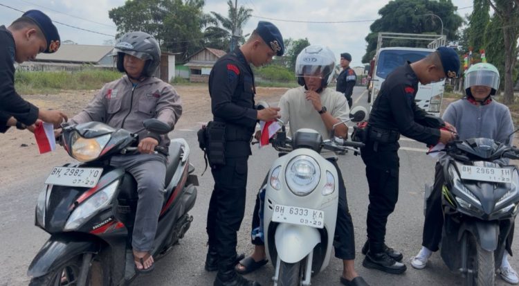Personel Brimob Polda Jambi membagikan bendera merah putih kepada pengendara motor di Muaro Jambi, Sabtu (2/8/2025). (Dok. Nahar)
