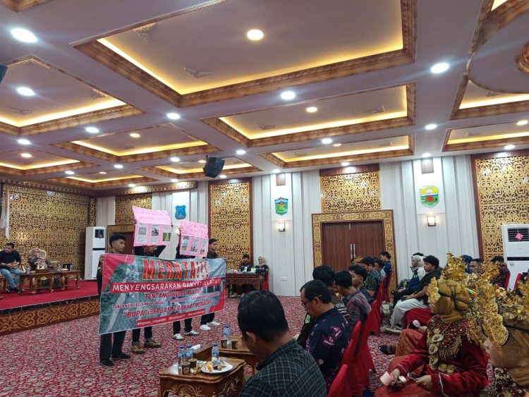 Empat mahasiswa membentangkan spanduk dan poster berisi tuntutan masyarakat terkait jalan rusak, pendidikan, dan kesehatan saat pelantikan Kapema Tanjung Jabung Timur di Balai Pertemuan Daerah, Minggu (21/9/2025). (Dok. Daus)