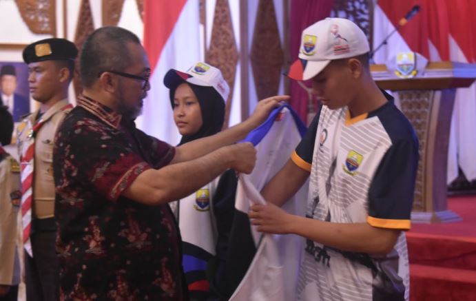 Sekretaris Daerah Provinsi Jambi Sudirman menyematkan atribut kepada salah satu atlet kontingen Jambi saat pelepasan peserta Pekan Olahraga Pelajar Nasional (POPNAS) XVII Tahun 2025 di Auditorium Rumah Dinas Gubernur Jambi, Kamis (30/10/2025). (Dok, Daus)