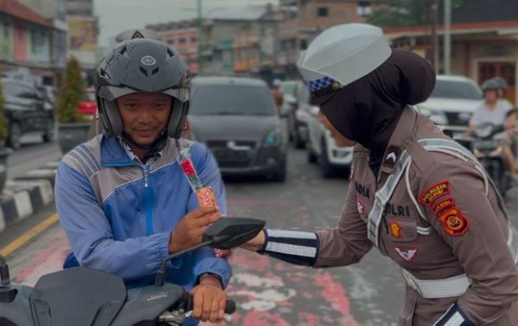Seorang personel Satlantas Polresta Jambi memberikan cokelat kepada pengendara di Simpang Jelutung, Kota Jambi, dalam rangka peringatan Hari Guru Nasional 2025, Selasa (25/11/2025). (Dok, Nahar)