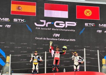 Pebalap muda Indonesia M. Kiandra Ramadhipa mengibarkan bendera Merah Putih di podium tertinggi usai menjuarai European Talent Cup (ETC) FIM JuniorGP 2025 di Circuit de Barcelona-Catalunya, Spanyol, Minggu (2/11/2025). (Dok. Sisnsen)