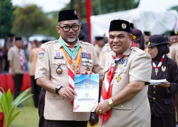 Sekda Provinsi Jambi, Sudirman, menerima buku laporan Gerakan Pramuka Kwartir Daerah Jambi dalam rangkaian Apel Besar Hari Pramuka ke-64 di Tanjung Jabung Timur, Rabu (19/11/2025). (Dok. Daus)