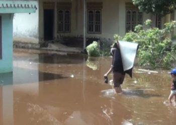 Seorang warga menggendong barang melintasi banjir yang menggenangi permukiman di Desa Kota Baru, Kecamatan Geragai, Kabupaten Tanjung Jabung Timur, akibat hujan deras dan pendangkalan sungai. (Dok. Daus)