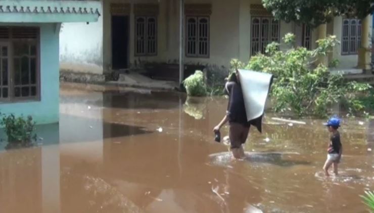 Seorang warga menggendong barang melintasi banjir yang menggenangi permukiman di Desa Kota Baru, Kecamatan Geragai, Kabupaten Tanjung Jabung Timur, akibat hujan deras dan pendangkalan sungai. (Dok. Daus)