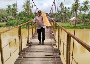 Kapolsek Limun AKP Berlin Tarigan bersama personel kepolisian dan warga mengangkat papan kayu untuk memperbaiki jembatan gantung di Desa Muara Limun, Kecamatan Limun, Kabupaten Sarolangun, Rabu (17/12/2025).-(Dok. Humas)