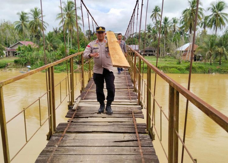 Kapolsek Limun AKP Berlin Tarigan bersama personel kepolisian dan warga mengangkat papan kayu untuk memperbaiki jembatan gantung di Desa Muara Limun, Kecamatan Limun, Kabupaten Sarolangun, Rabu (17/12/2025).-(Dok. Humas)
